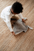 A young child with curly hair and a white shirt picks up the Senger Naturwelt Stuffed Animal - Large Manta Ray from a woven, tan-colored rug.