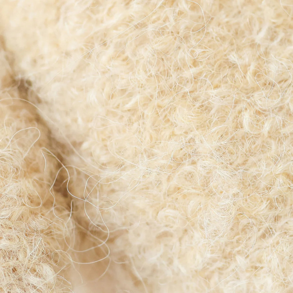 Close-up of cream-colored, curly wool fibers from the Cuddle + Kind Baby Bouclé Bear - Honey, showcasing a soft and fluffy texture with fine strands visible throughout.