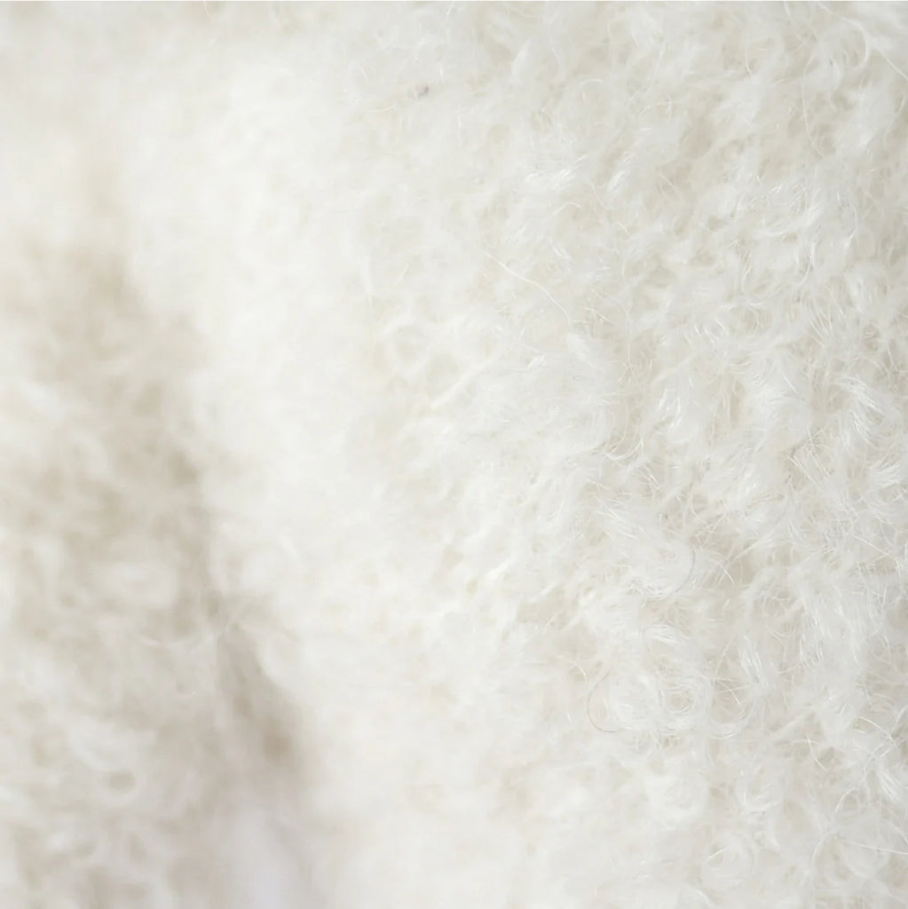 Close-up of the soft, curly textured fibers of the Cuddle + Kind Baby Bouclé Bear - Ivory, showcasing its cozy off-white plush reminiscent of collectible toys made from Peruvian alpaca yarn.