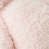 Close-up of the Cuddle + Kind Baby Bouclé Bear - Strawberry, featuring soft, light pink curly bouclé fabric with a fluffy, cozy hand-knit appearance.