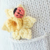Close-up of Cuddle + Kind Beatrice The Mouse - Periwinkle, featuring a knitted yellow flower with a small red and black ladybug on light gray fabric; handmade with sustainable fair trade practices.