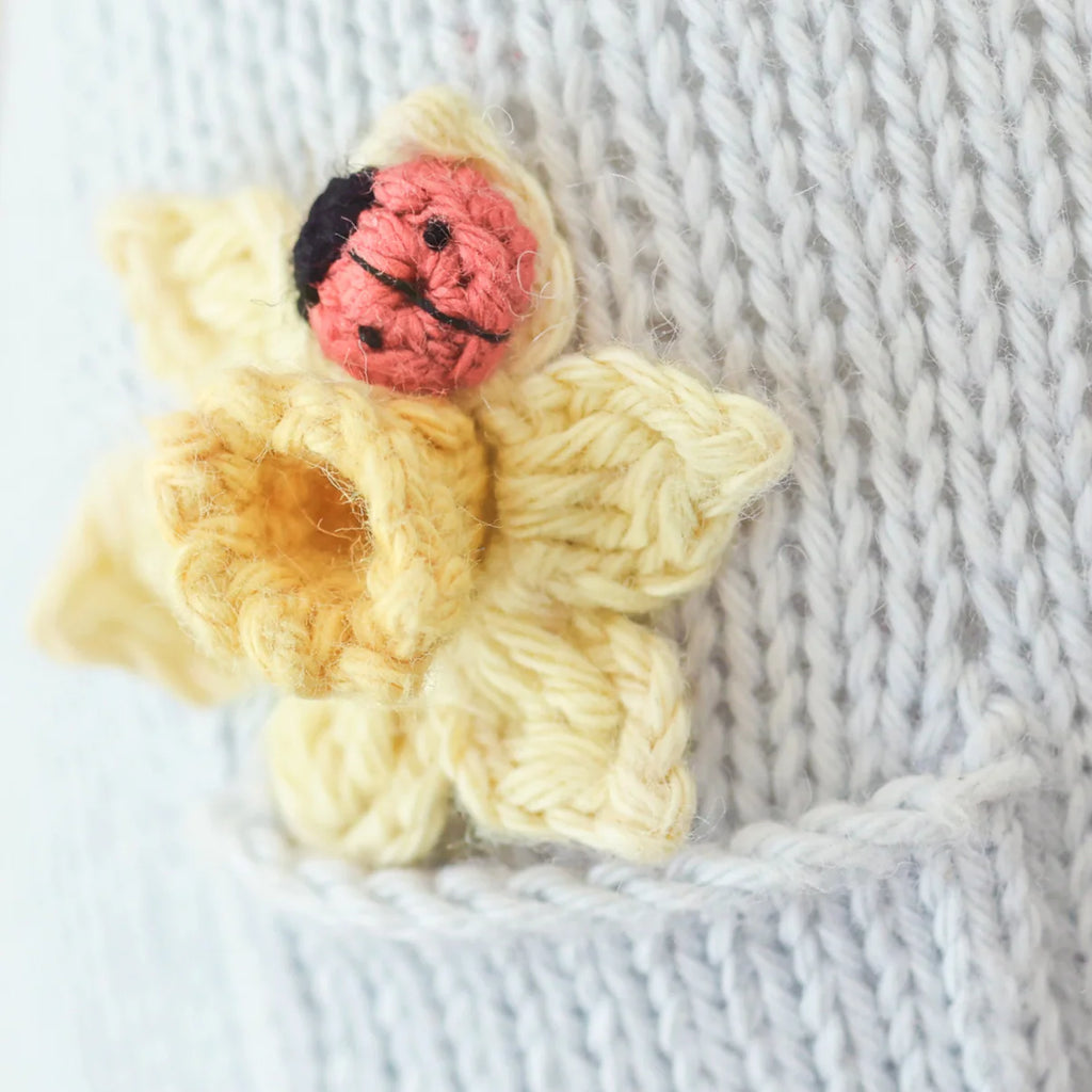 Close-up of Cuddle + Kind Beatrice The Mouse - Periwinkle, featuring a knitted yellow flower with a small red and black ladybug on light gray fabric; handmade with sustainable fair trade practices.