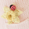 A close-up of Cuddle + Kind Beatrice The Mouse - Blush shows a knitted yellow cotton flower with a red and black ladybug decoration on soft light pink knit fabric.