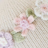 Close-up of Cuddle + Kind Emma The Mouse’s knitted beige fabric, adorned with pastel pink, white, and lavender crocheted flowers and green leaves—crafted from hypoallergenic materials for comfort and safety.