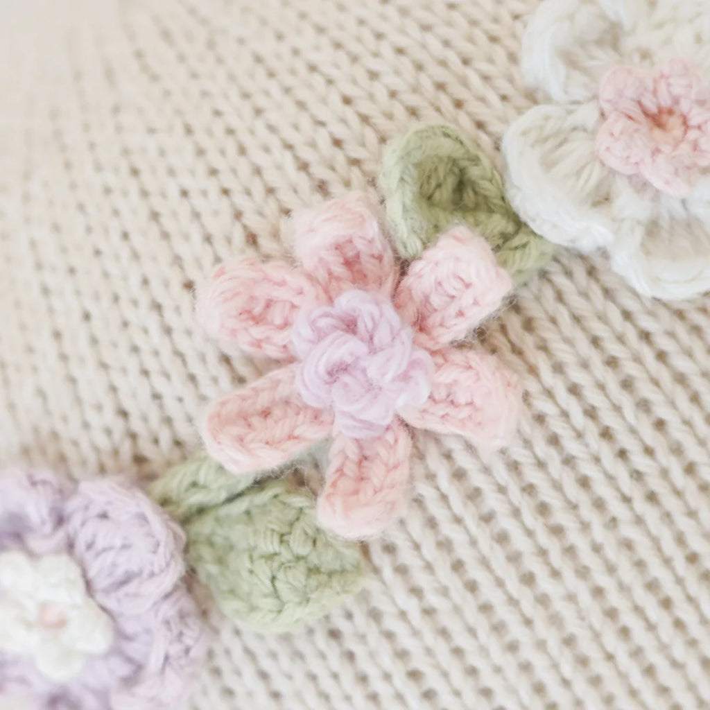 Close-up of Cuddle + Kind Emma The Mouse’s knitted beige fabric, adorned with pastel pink, white, and lavender crocheted flowers and green leaves—crafted from hypoallergenic materials for comfort and safety.