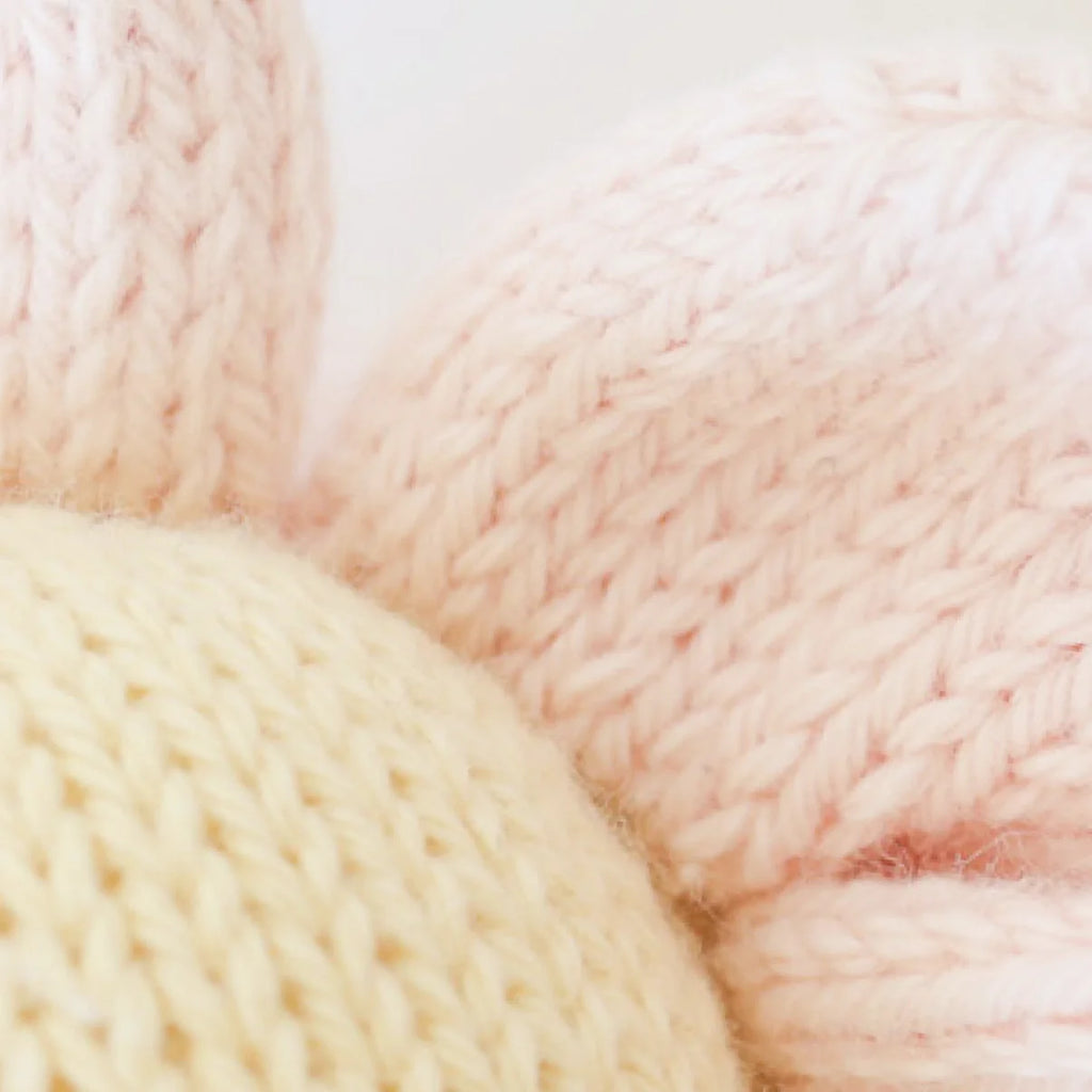 Close-up of Cuddle + Kind Baby Daisy - Blush Pink, featuring soft, fair trade, hand-knit fabric in cream and blush from natural Peruvian cotton yarn—cozy textured threads evoke lovingly crafted baby animals.