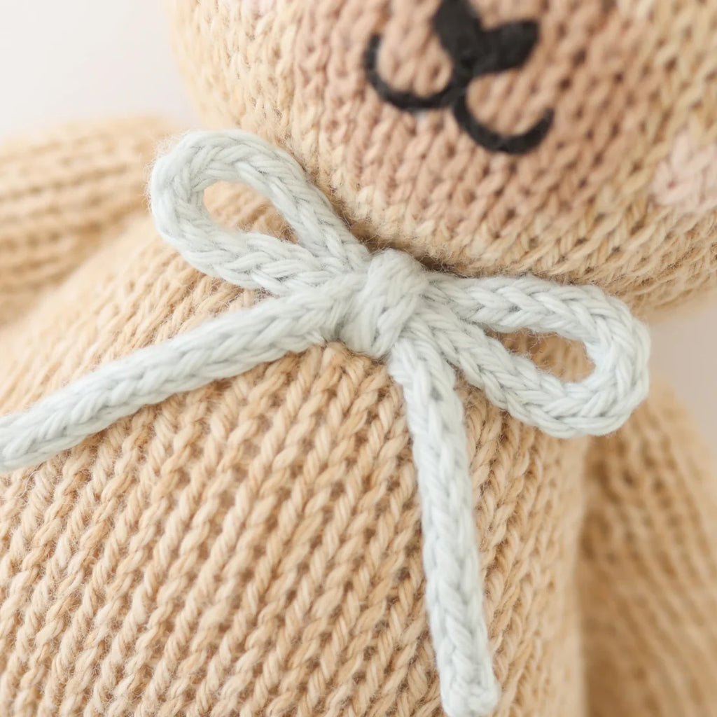Close-up of the Cuddle + Kind Baby Honey Bear in Robin’s Egg Blue, hand-knit in Peru from natural Peruvian cotton yarn, featuring a light blue bow and visible textured stitches.