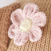 Close-up of Cuddle + Kind Bea The Dog featuring a hand-knit pink flower with a cream-colored center, attached to a brown knitted background.