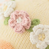 Close-up of Cuddle + Kind Duckling’s knitted fabric featuring pink and white crocheted flowers with green leaves on a soft yellow background, ideal for handmade dolls filled with hypoallergenic polyfill.