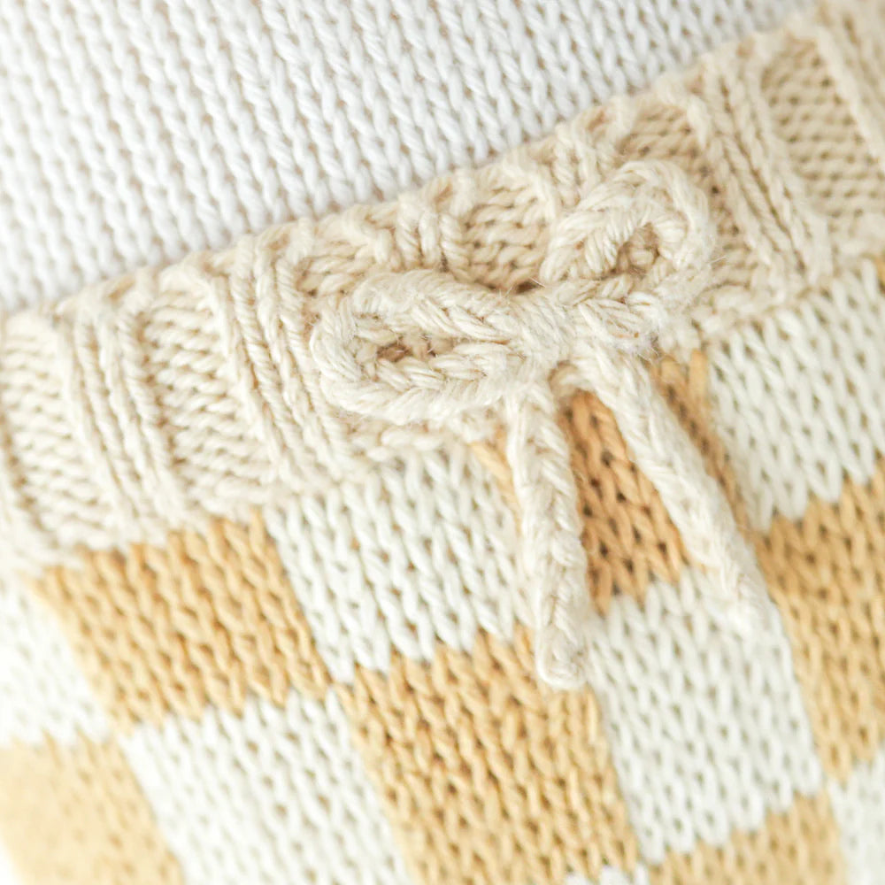 Close-up of Cuddle + Kind George The Dog’s hand-knit fabric, featuring a cream bow on a ribbed band and a yellow and white checkered pattern—crafted with sustainable, fair trade practices.