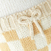 Close-up of Cuddle + Kind George The Dog’s hand-knit fabric, featuring a cream bow on a ribbed band and a yellow and white checkered pattern—crafted with sustainable, fair trade practices.