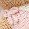 Close-up of Cuddle + Kind Bea The Dog, showcasing soft hand-knit fabric with a light pink bow against a pink, cream, and beige yarn background, highlighting the detailed knit stitches and texture.