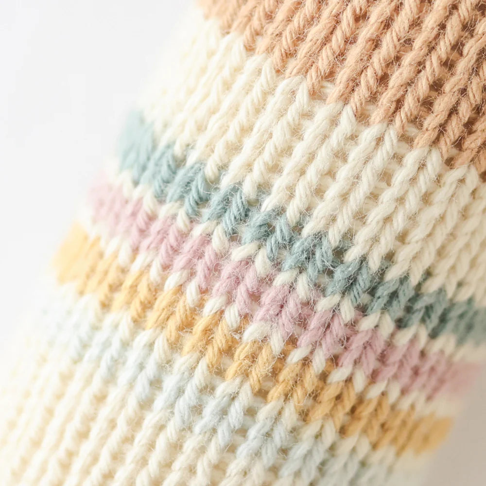 Close-up of Cuddle + Kind George The Dog’s hand-knit fabric, featuring cream, tan, blue, yellow, and pink stripes with detailed stitches—expertly crafted using sustainable fair trade practices.
