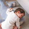 A smiling young child hugs a Ride-On Whale Pouf on a striped carpet, with another plush whale floor cushion in the background.