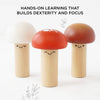 Three smiling wooden mushrooms with colorful caps stand together. Text above reads, "Woodland Mushroom Hammer Game: Hands-on learning that builds fine motor skills, dexterity, and focus.