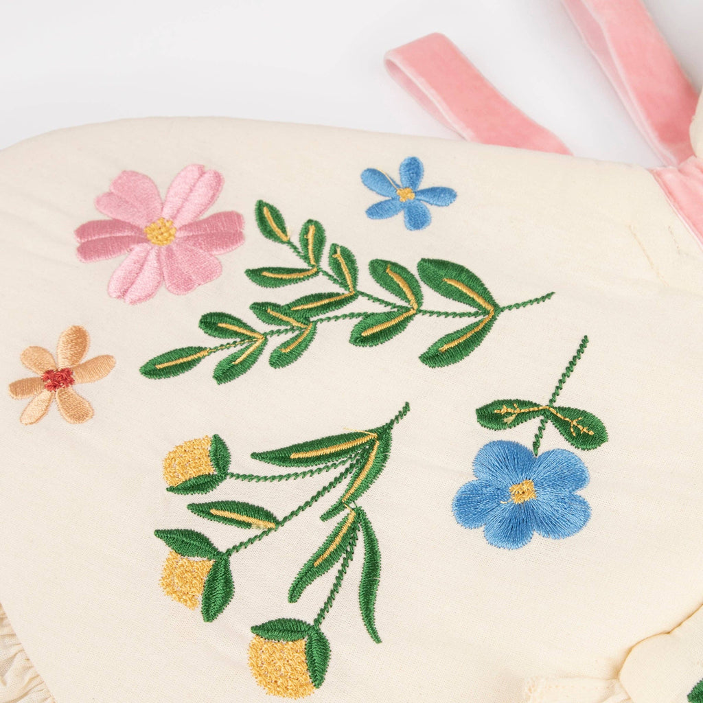 Meri Meri Butterfly Wings feature cream-colored natural cotton with embroidered pink, blue, yellow, and green flowers and leaves, plus pink fabric straps at the top right corner.