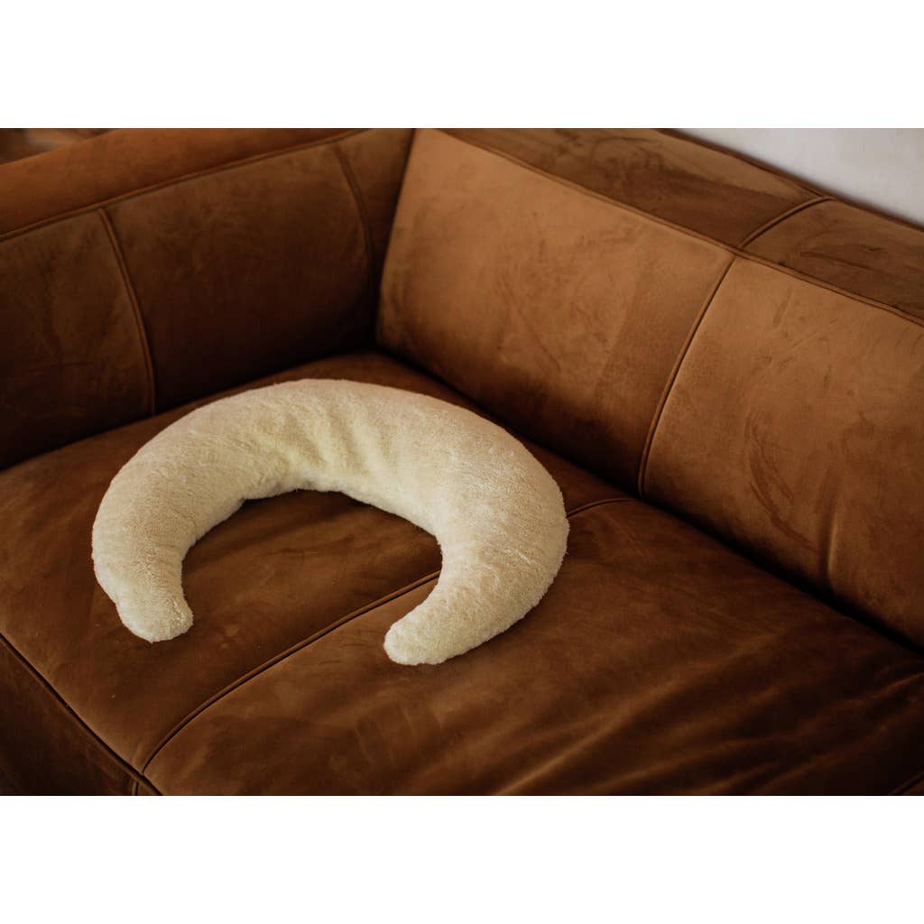 The Senger Naturwelt - Moon Nursing and Neck Pillow, with its ergonomic crescent shape, rests on a brown suede couch.