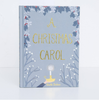 The "A Christmas Carol | Collector's Edition| Hardcover Book" features gold lettering, winter branches, holly, and a glowing lamp—inviting you into Ebenezer Scrooge’s world—on a light grey-blue cover.