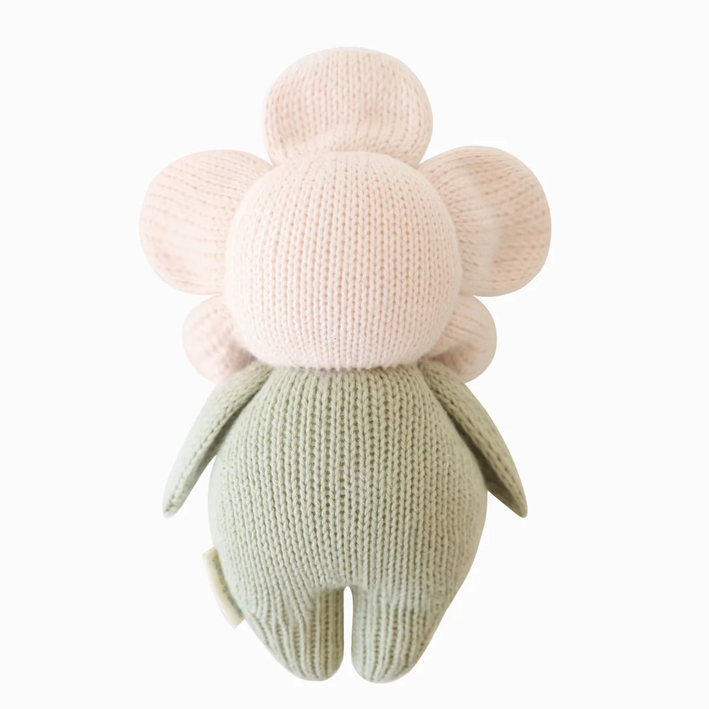 The Cuddle + Kind Baby Daisy - Blush Pink is a hand-knit plush toy crafted from natural Peruvian cotton yarn, with a round pink flower head and green body, shown from the back on a white background.