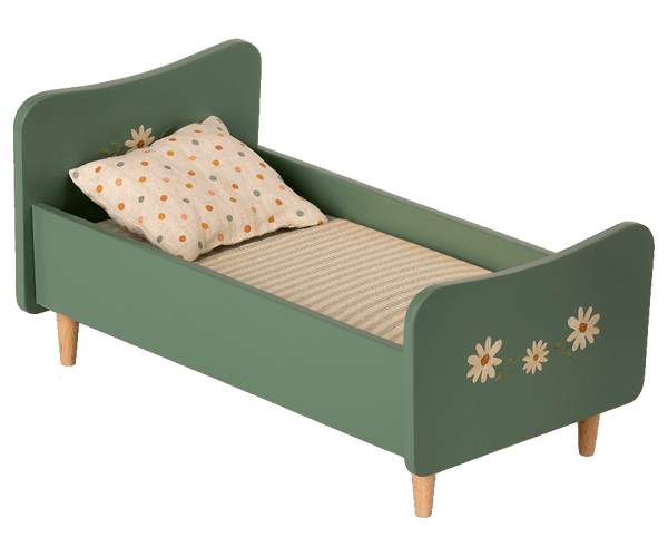 A small green wooden Maileg Wooden Bed, Mini with handpainted floral decorations and charming bunnies on the headboard and footboard. The bed has a beige mattress with thin stripes and a white pillow with brown polka dots. It stands gracefully on four short wooden legs.