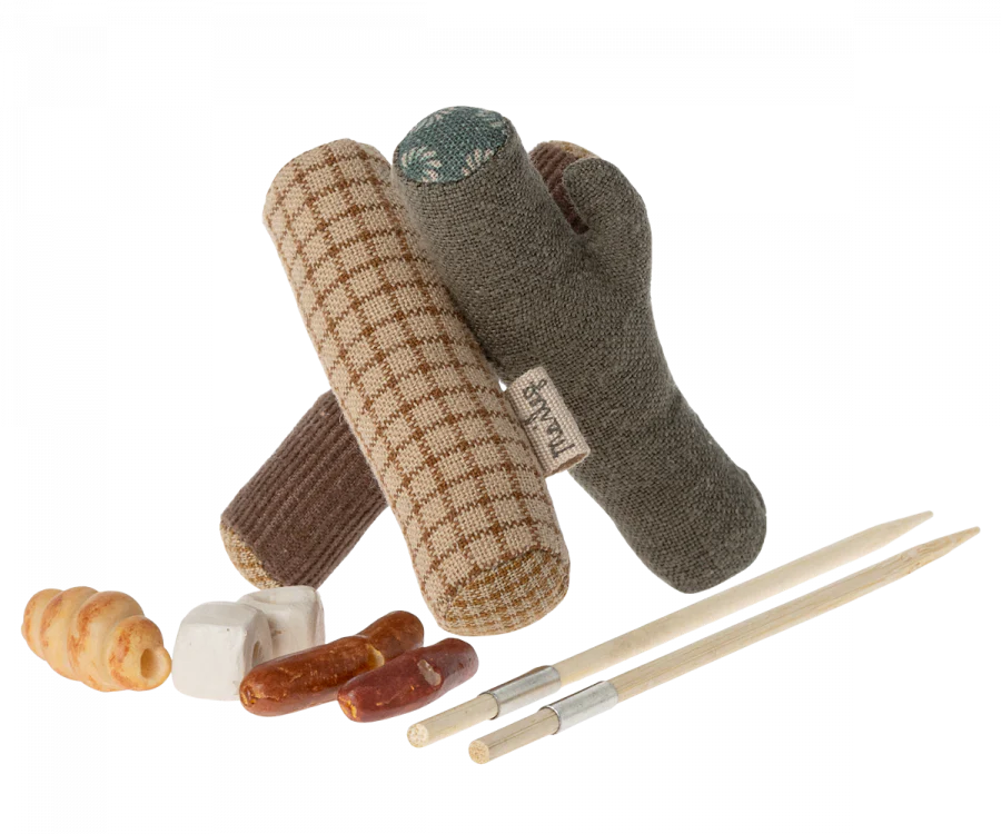 The Maileg Camping Set includes three soft toy logs in a pyramid shape, like a bonfire, two chew sticks with white ends, and assorted colorful bone and roll treats. Perfect for sparking your pup's sense of adventure!.