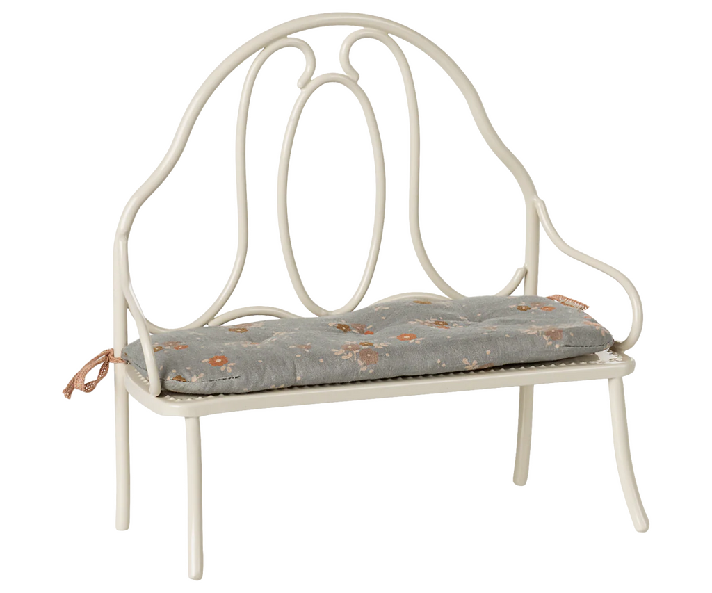 The Maileg Vintage Bench, Miniature - Off White features a decorative rounded backrest and a blue-gray floral cushion tied to the frame. Perfectly sized for bunny and rabbit spaces, it adds vintage charm and comfort to any mini setting.