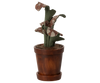 The Maileg Flower Pot With Plant, Miniature features green and brown floral-patterned leaves in a wooden pot, set against a blurred striped background.