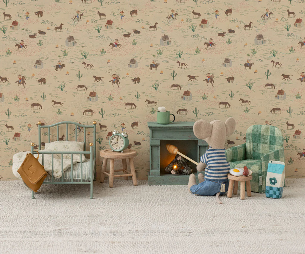 A cozy miniature Mouse hole Farmhouse scene features a bed, nightstand, clock, table, fireplace, and the Maileg Folding Chair, Mouse - Green Checker. A Maileg mouse toy in a striped shirt sits by the fire with tiny food; animal wallpaper adds charm.