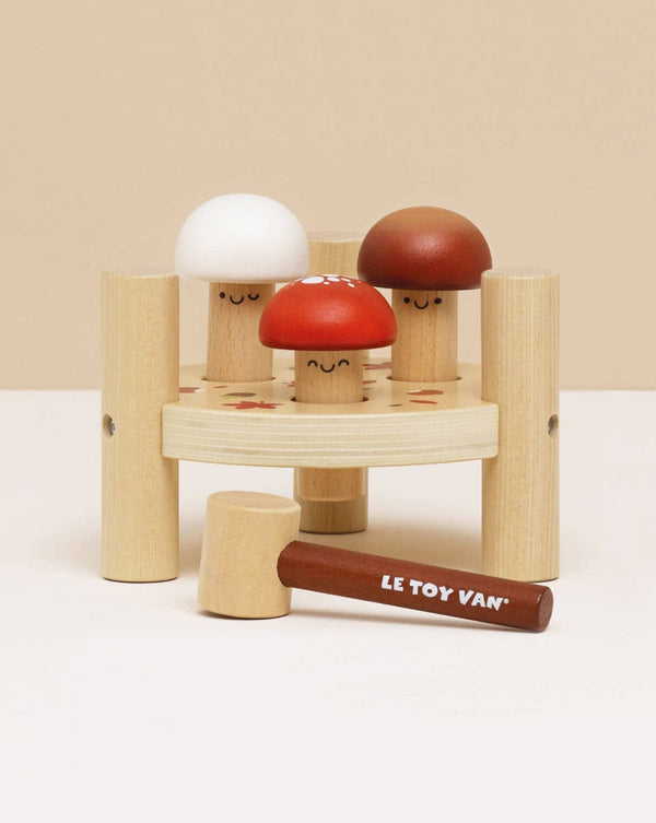 The Woodland Mushroom Hammer Game features three smiling mushroom pegs—white, red, and brown—in a circular base. Includes a Le Toy Van mallet for playful fine motor skill development.
