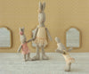 Three Maileg Rabbit, Micro - Ballet Suit and Skirt, Cream stand on a textured surface. Set against yellow patterned wallpaper and three small mirrors, the rabbits are posed like playful ballet dancers in pastel skirts.