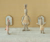 Three Maileg Rabbit, Size 1 - Classic - Ballet Suit and Skirt - Cream toys in pastel tutus stand on a textured surface before a patterned yellow wall with three small mirrors, striking playful poses as if mid-dance.