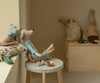 Stuffed animal toys, including a mouse, dog, and rabbit, are arranged around a small table topped with the Maileg Cushion - Pony in a cozy children's room. Small toy dishes and pastries decorate the scene.