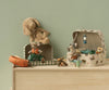 Two toy mice are ready for play in the Maileg Suitcase Set, 2-Pieces - Pony: one rides a scooter while the other relaxes with camping gear. A plush dog rests on a storage suitcase, all arranged on wood against a pale green wall.