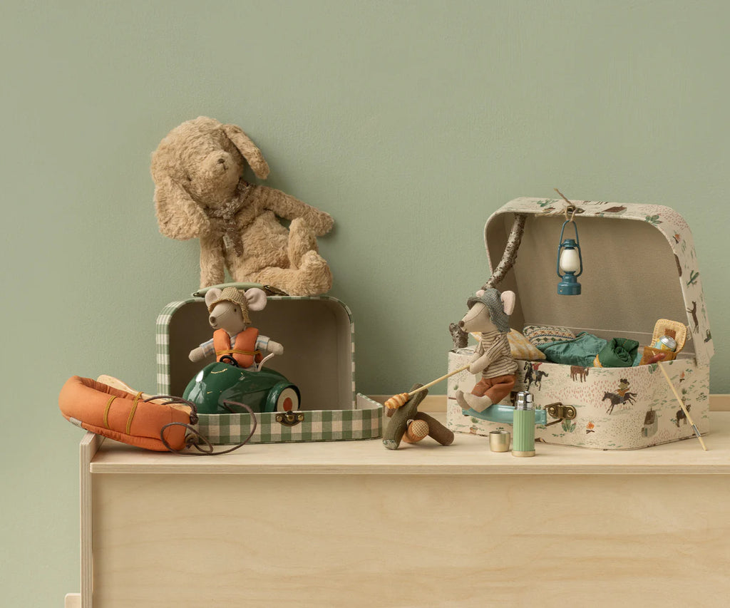 Two toy mice are ready for play in the Maileg Suitcase Set, 2-Pieces - Pony: one rides a scooter while the other relaxes with camping gear. A plush dog rests on a storage suitcase, all arranged on wood against a pale green wall.