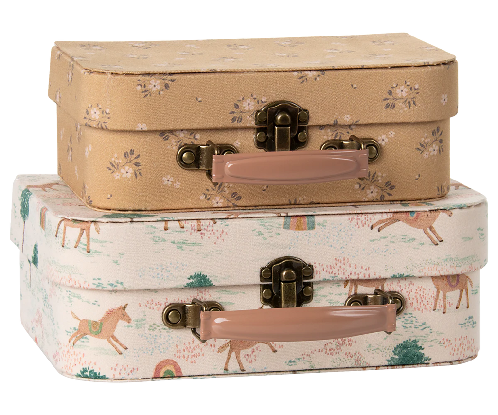 The Maileg Suitcase Set, 2-Pieces - Unicorn, includes two decorative cases: the top is light brown with white flowers, while the bottom features unicorns, trees, rainbows, and is finished with light pink handles and brass clasps.
