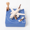 A Airport Music Box toy airplane on a blue, runway-themed play mat complete with small buildings, a control tower, and a vehicle. The setup is designed to simulate an airport environment.