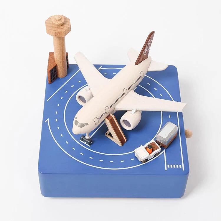 A Airport Music Box toy airplane on a blue, runway-themed play mat complete with small buildings, a control tower, and a vehicle. The setup is designed to simulate an airport environment.