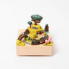 A Wooden Train Music Box - Spring scene featuring a train track winding around miniature trees, buildings, and a tunnel, all arranged on a square wooden base.