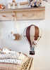 A small stuffed mouse sits in the Hot Air Balloon - Light Brown / Dark Brown, hanging in a cozy nursery with folded blankets, a toy airplane, and a wooden camera—perfect as a charming children’s room decoration.