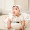 A baby in a cream outfit lies on their stomach, gazing upward with curiosity, hands resting on the Tummy Time Palette—a tummy time pillow featuring colorful patches—while on a soft mat.