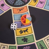 A close-up of the 3-in-1 Game Collection: Scrabble, Trivial Pursuit & Cribbage shows the Trivial Pursuit game piece with colorful wedges and a die, evoking classic tabletop fun while highlighting different question categories with icons.