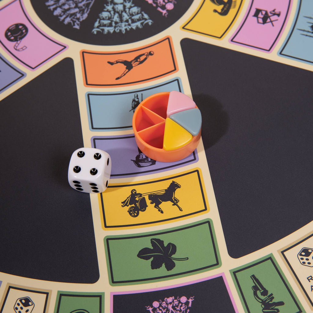 A close-up of the 3-in-1 Game Collection: Scrabble, Trivial Pursuit & Cribbage shows the Trivial Pursuit game piece with colorful wedges and a die, evoking classic tabletop fun while highlighting different question categories with icons.