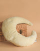 The Senger Naturwelt - Moon Nursing and Neck Pillow, plush and crescent-shaped, rests against a closed wicker basket on a beige background.