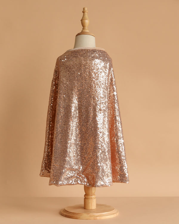 A child-sized mannequin showcases the Cape - Pink sequins against a plain beige background, with the sparkling pink costume draping elegantly from shoulders to mid-calf.