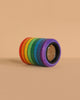 The Mader Rainbow Kaleidoscope, featuring adhesive tape rolls in red, orange, yellow, green, blue, and purple, is stacked on a beige surface and background for a vibrant display reminiscent of a kaleidoscope lens.