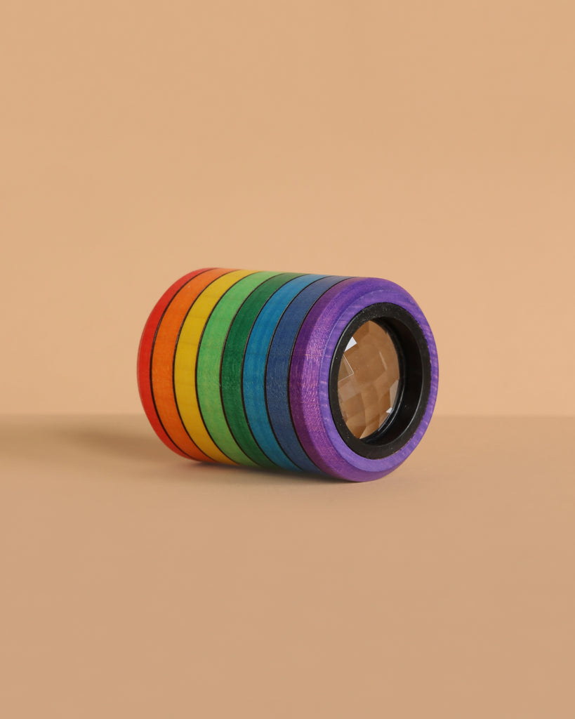 The Mader Rainbow Kaleidoscope, featuring adhesive tape rolls in red, orange, yellow, green, blue, and purple, is stacked on a beige surface and background for a vibrant display reminiscent of a kaleidoscope lens.