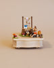 A whimsical miniature scene featuring a small Wooden Bunny Music Box celebrating a birthday with a cake and gifts on a tiny wooden table, crafted from sustainably sourced wood, set against a neutral background.