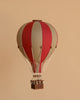 The Hot Air Balloon - Burgundy features a handmade design in red and beige with a small wicker basket, suspended against a light brown background—an ideal decoration for any child's room.