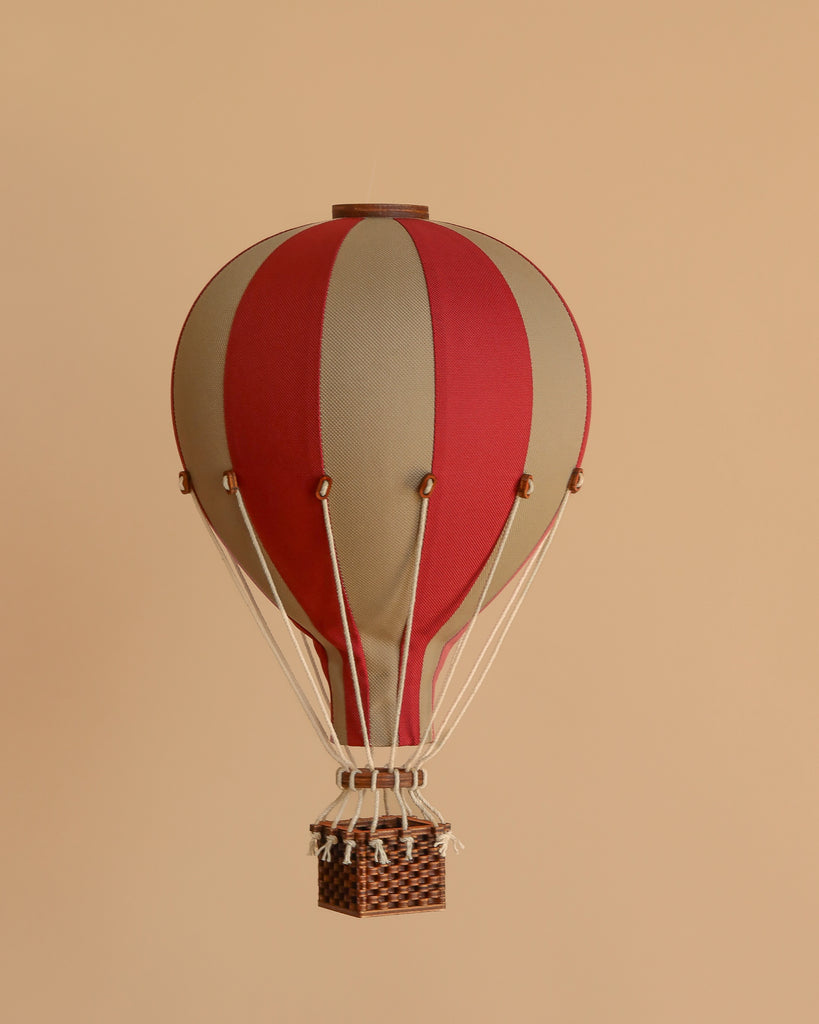 The Hot Air Balloon - Burgundy features a handmade design in red and beige with a small wicker basket, suspended against a light brown background—an ideal decoration for any child's room.