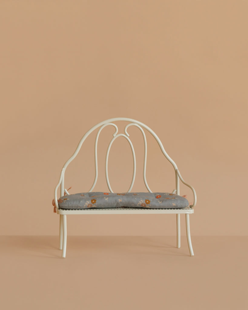 The Maileg Vintage Bench, Miniature - Off White features a decorative backrest and a light blue floral cushion, ideal for displaying Maileg bunnies or teddy bears against any background.